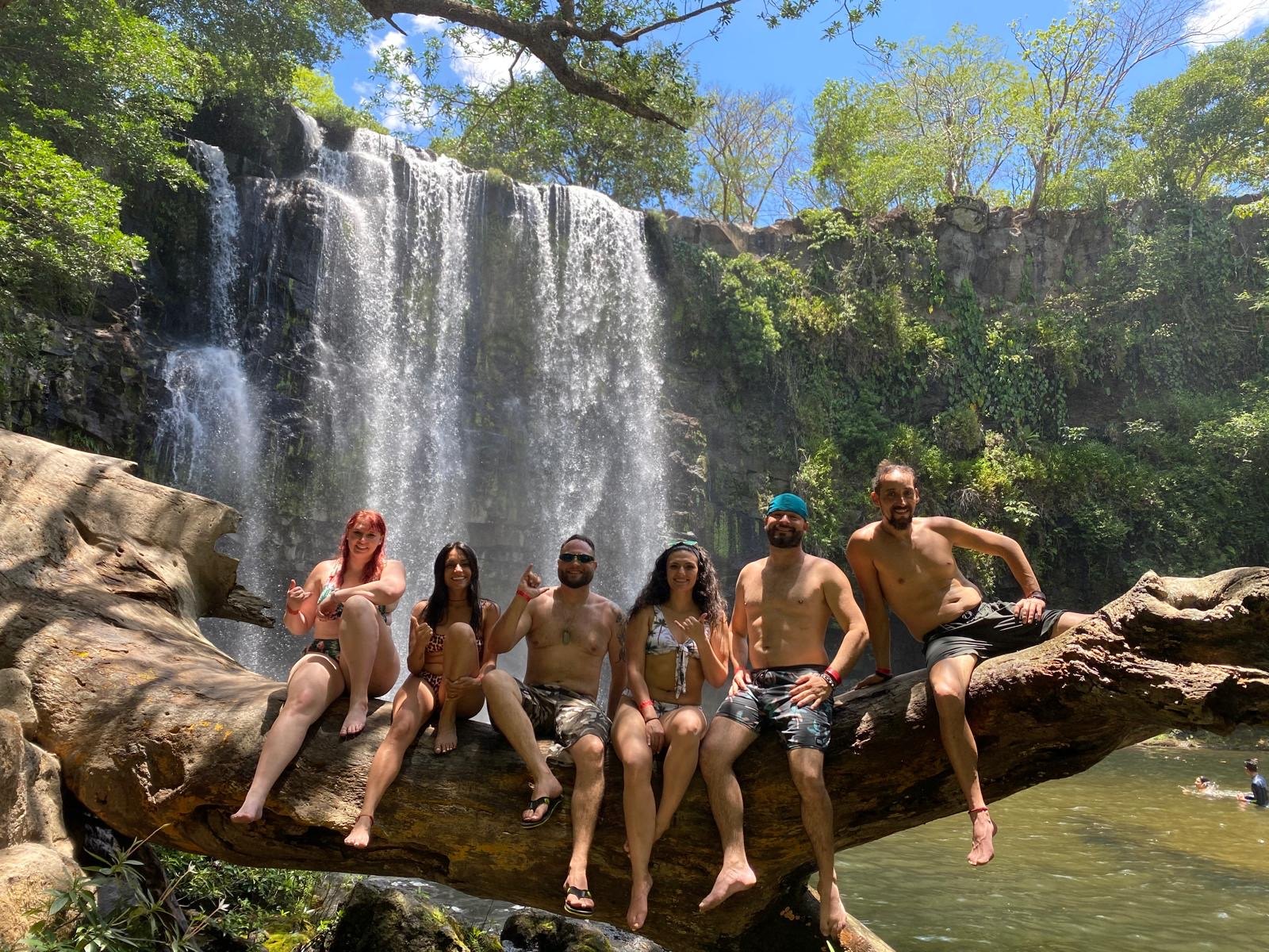 A group of travelers together on a log in front of a Costa Rican waterfall